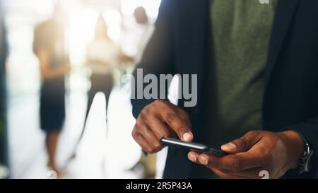 Er ist der, mit dem jeder Kontakt aufnehmen möchte. Nahaufnahme eines unbekannten Geschäftsmanns, der ein Handy in einem Büro mit seinen Kollegen benutzt Stockfoto