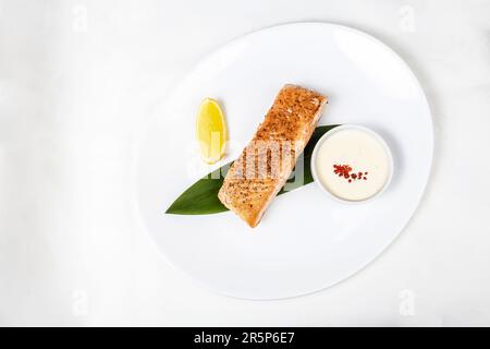 Ein Teller mit gegrilltem Fisch mit Zitrone und geröstetem Gemüse, ein klassisches Restaurantgericht zum Mittag- oder Abendessen. Stockfoto