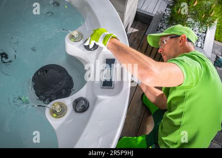 Techniker im kaukasischen Garten in seinem 40s. Er führt saisonale Wartung des Wannen-Whirlpools durch Stockfoto