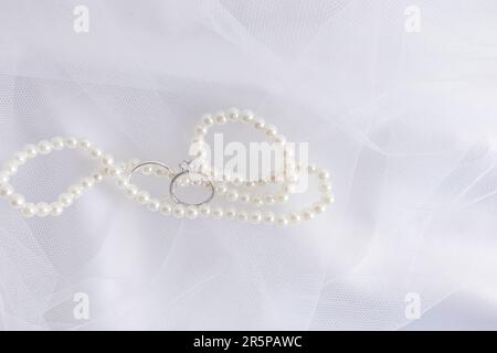 Ein schicker Hintergrund für Hochzeitsdesign. Eine elegante weiße Perlenkette und zwei weiße goldene Verlobungsringe Stockfoto