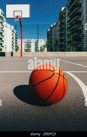 Basketballball auf einem Freiluftplatz mit Betonoberfläche und Backboard mit Basketballkörben im Hintergrund im Wohnviertel, selektiver Fokus Stockfoto