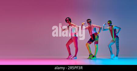 Drei Männer im farbenfrohen Retro-Sportswear-Training, die Aerobic-Übungen vor einem blau-rosa Studiohintergrund machen Stockfoto