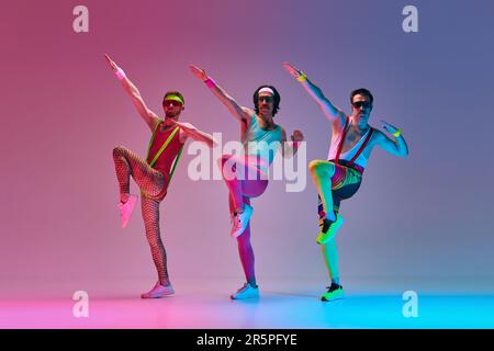 Sportliche, lustige Männer im farbenfrohen Retro-Sportswear-Training, die Übungen vor einem abgestuften, rosa Studiohintergrund in Neonlicht machen Stockfoto