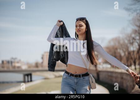 Die schöne brünette Frau hängt mit ihrem Freund ab. Er hält ihre Hand, während sie über die Kaiwand läuft Stockfoto