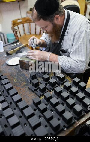 Ein orthodoxer jüdischer Handwerker bereitet Tefillinboxen zu, die mit den erforderlichen handgeschriebenen Pergamenten geführt werden. In einem Laden in Brooklyn, New York. Stockfoto