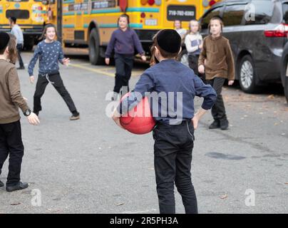 Während der Pause ihrer Jeschiwa-Schule spielen orthodoxe jüdische Schüler in Schädelkappen in einer abgeschlossenen Straße. In Brooklyn, New York. Stockfoto