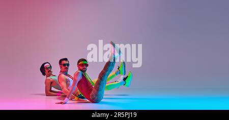 Männer in farbenfroher Sportbekleidung im Retro-Look machen Aerobic-Übungen vor einem abgestuften, rosa Studiohintergrund. Flexibilität Stockfoto