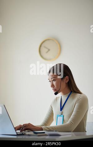 Geschäftsfrau, die ein Headset trägt, wenn sie in einem modernen Büro mit einem Laptop arbeitet Stockfoto