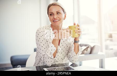Es geht nichts über eine frische Tasse Kaffee, um den Tag zu beginnen. Eine reife Geschäftsfrau, die von ihrem Heimbüro aus arbeitet. Stockfoto