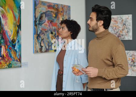 Ein multiethnisches Paar, das sich Gemälde an der Wand ansieht, während es die Kunstgalerie besucht Stockfoto