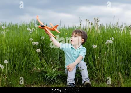 Ein Kind träumt davon, Pilot zu werden und spielt mit einem orangefarbenen Flugzeug Stockfoto