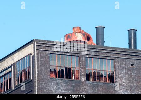 Eine Nahaufnahme eines zerbrochenen Fensters in einer Ziegelmauer mit Schmutz, der um den Rahmen verstreut ist Stockfoto