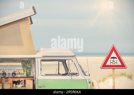 Seitlicher Blick auf ein Wohnmobil aus den 70er Jahren und Picknickschild vor einem Strand mit blauem Himmel Stockfoto