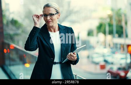 Die erfolgreichen haben eine Vision. Porträt einer erwachsenen Geschäftsfrau, die draußen auf dem Balkon eines Büros steht und ein digitales Tablet in der Hand hält. Stockfoto