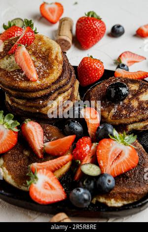 Ein appetitlicher Stapel flauschiger Pfannkuchen, garniert mit einer Auswahl an frischem Obst und Beeren, serviert auf einem Teller Stockfoto