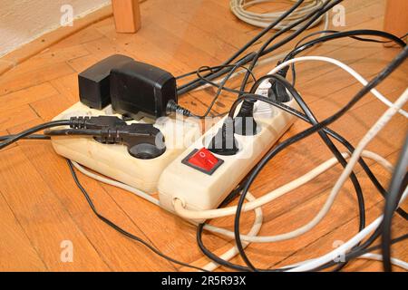 Verwickelte Kabel auf dem Parkettboden. Überlastete Schalttafeln auf dem Holzboden. Elektrische Kabel bei Störungen. Stockfoto