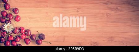 Panoramablick von oben auf Kirschen und Gänseblümchen auf Holzhintergrund mit Kopierbereich Stockfoto