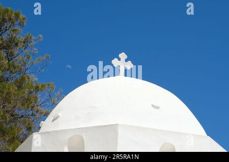 Ein Kreuz auf der Spitze einer orthodoxen, weiß getünchten Kirche in iOS Griechenland und ein blauer Himmel im Hintergrund in iOS Griechenland Stockfoto