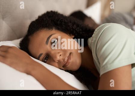 Lächelnde junge Frau, die mit ihrem Mann im Bett lag Stockfoto