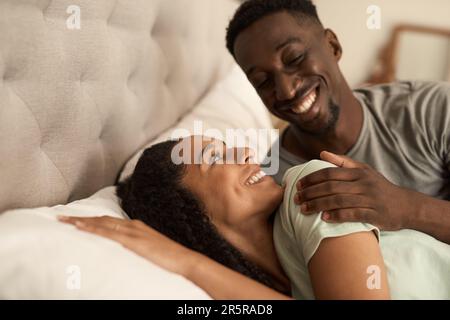 Lächelndes, junges, multiethnisches Paar, das morgens im Bett aufwacht Stockfoto