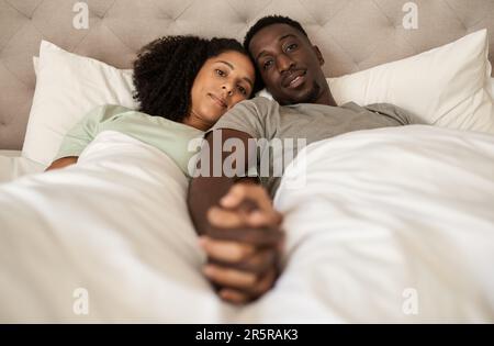 Liebevolles, junges, multirassisches Paar, das Hände im Bett hält Stockfoto