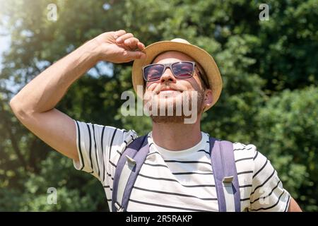 Junger erwachsener Mann mit Strohhut und Sonnenbrille, der im Sommer einen sonnigen Tag im Freien genießt. Stockfoto
