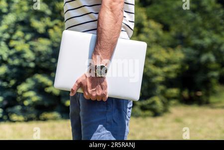 Zeitsparendes und tragbares Konzept, männlicher Mensch mit Uhr am Handgelenk hält Laptop in der Hand. Stockfoto