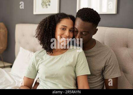 Lächelndes, junges, multirassisches Paar, das morgens in seinem Schlafzimmer sitzt Stockfoto