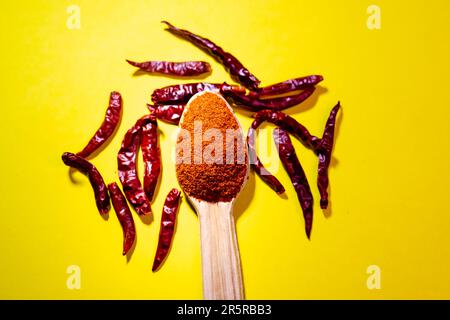 Nahaufnahme eines Löffels mit getrocknetem rotem Pfeffer und Chiliflocken auf hellgelbem Hintergrund Stockfoto