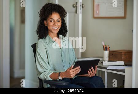 Lächelnde junge Geschäftsfrau, die ein Tablet in ihrem Heimbüro verwendet Stockfoto