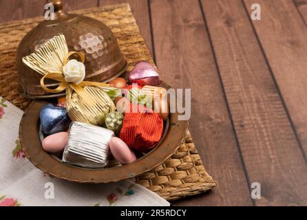 Nahaufnahme einer antiken Kupferschale mit Süßigkeiten. Gewickelte Schokolade und Mandeldragee auf dem Holztisch. Kopierbereich. ramadan Festgottesdienst. Stockfoto