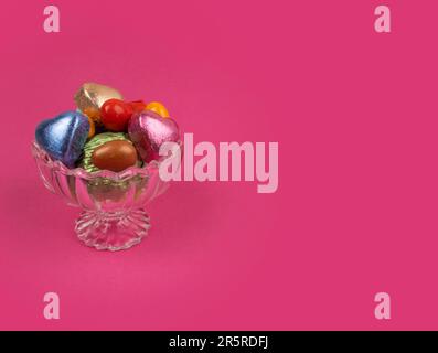 Luxuriöse Pralinen in einer Glasschale. Isolierter rosafarbener Hintergrund mit Kopierraum. Das Zuckerfest-Konzept. Mandelbonbons in stilvoller Kristallschleife. Stockfoto