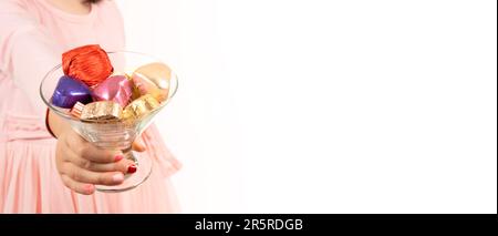 Mädchen, das eine Glasschale mit Süßigkeiten hält. Mit umhüllter, farbenfroher Schokolade. Traditionelles ramadan-Festkonzept mit Bannerdesign. Isolierter weißer Hintergrund. Stockfoto