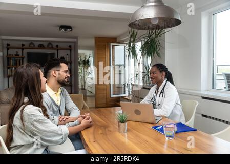 Eine Ärztin besucht ein junges Ehepaar zu Hause und gibt Gesundheitsberatungen. Arzthelferin in einer Patientenwohnung, die zuhört Stockfoto