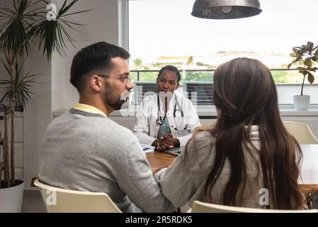 Eine Ärztin besucht ein junges Ehepaar zu Hause und gibt Gesundheitsberatungen. Arzthelferin in einer Patientenwohnung, die zuhört Stockfoto