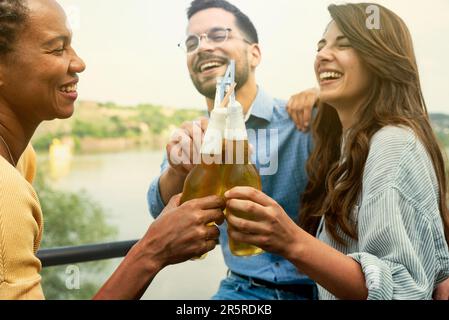 Eine Gruppe glücklicher junger, multiethnischer Freunde, Freiberufler in lässiger Kleidung, trinken kaltes Bier und tanzen zusammen, während die Party im Gebäude stattfindet Stockfoto