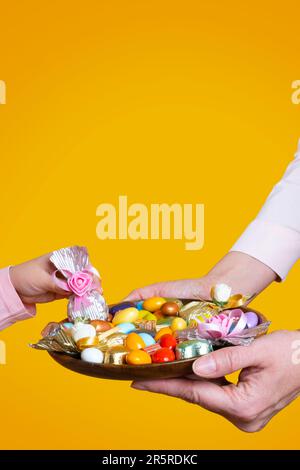 Idee eines Festkonzepts. Gelber Studiohintergrund, Kopierraum. Mädchen, das Luxus-Schokolade in der Hand nimmt. Traditionelle türkische ramadan- oder Ramazan-Süßigkeiten. Stockfoto