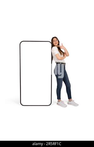 Frau, die auf ein riesiges Smartphone-Mockup mit leerem weißen Bildschirm zeigt, eine kaukasische schöne Dame, die ein riesiges Handy stützt. Stockfoto