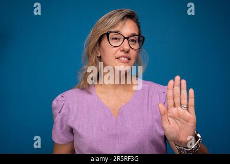 Hübsche Brasilianerin, blond, trägt eine lila Krankenschwester-Uniform und macht mit einer Hand Halt. Positive Person. Isoald auf blauem Hintergrund. Stockfoto