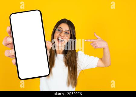 Aufgeregte weiße Dame, die mit dem Finger auf ihr Smartphone zeigt, um ein tolles Angebot für Mobilgeräte zu erhalten. Ein Mobiltelefon mit leerem Bildschirmfoto. Stockfoto
