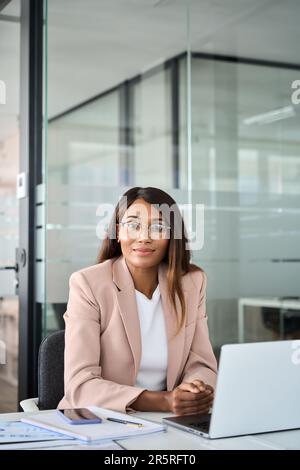 Selbstbewusste junge Anwältin im Büro sitzt am Schreibtisch, vertikales Porträt. Stockfoto