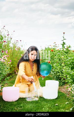 Frau spielt Musik auf Kristallschüsseln, entspannt sich in einem wunderschönen grünen Garten Stockfoto