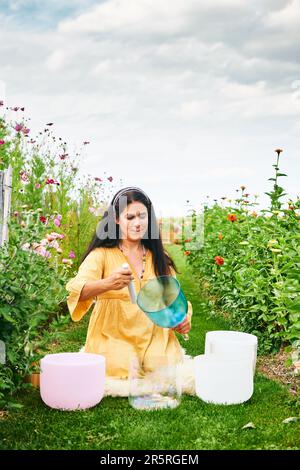 Frau spielt Musik auf Kristallschüsseln, entspannt sich in einem wunderschönen grünen Garten Stockfoto