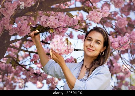 Schöne lächelnde Frau vor dem Hintergrund von lila rosa Kirschblüten Stockfoto