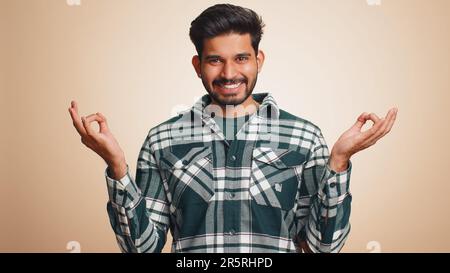 Beruhige dich, entspann dich, innere Balance. Der junge indianer atmet tief ein mit Mudra-Geste, Augen geschlossen, meditiert mit konzentrierten Gedanken, friedlicher Geist. Hindu-Typ isoliert auf beigefarbenem Hintergrund Stockfoto