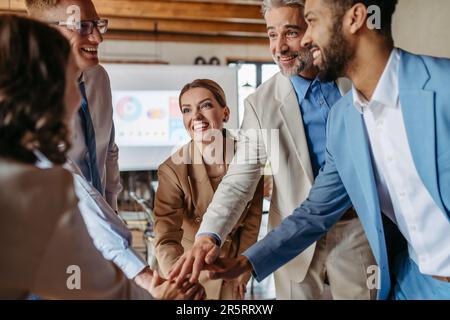 Glückliches Business-Team, das Hände zusammenstapelt, um sich aufzuheitern, während sie lachen und ihren Erfolg feiern. Stockfoto