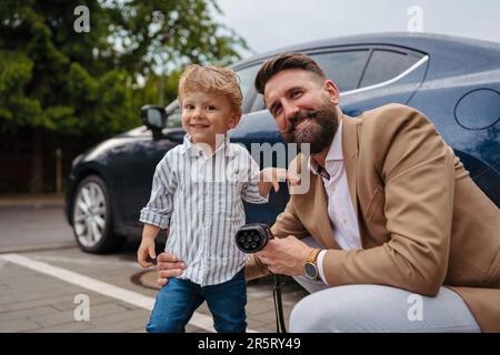 Nahaufnahme eines Mannes und seines kleinen Sohnes, die das Stromversorgungskabel aus ihrem Elektroauto halten. Stockfoto