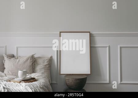 Elegante Innenausstattung des Schlafzimmers. Vertikales Holzmodell mit Bilderrahmen auf einem modernen, organisch geformten Beistelltisch. Tasse Kaffee auf dem Tablett. Frühstück im Bett Stockfoto