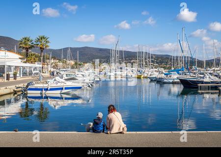 Frankreich, Var, Cavalaire-sur-Mer, Mutter und ihr kleines Kind sitzen auf einem Kai mit Blick auf den Hafen von Cavalaire Stockfoto