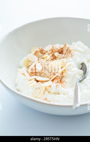 Hüttenkäse mit Zimt und Mandeln in einer weißen Schüssel, weißer Hintergrund. Gesundes Proteinfrühstück-Konzept. Stockfoto